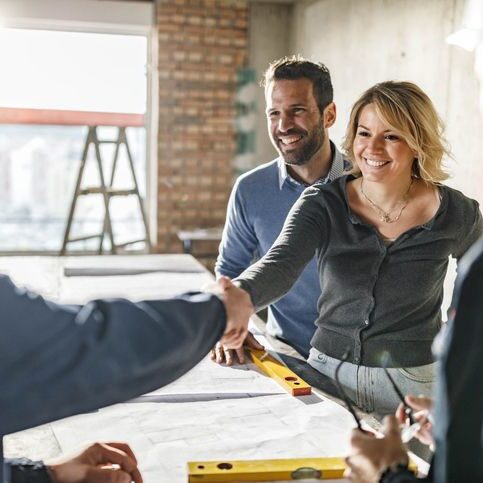 Happy couple came to an agreement with their building contractors at construction site.